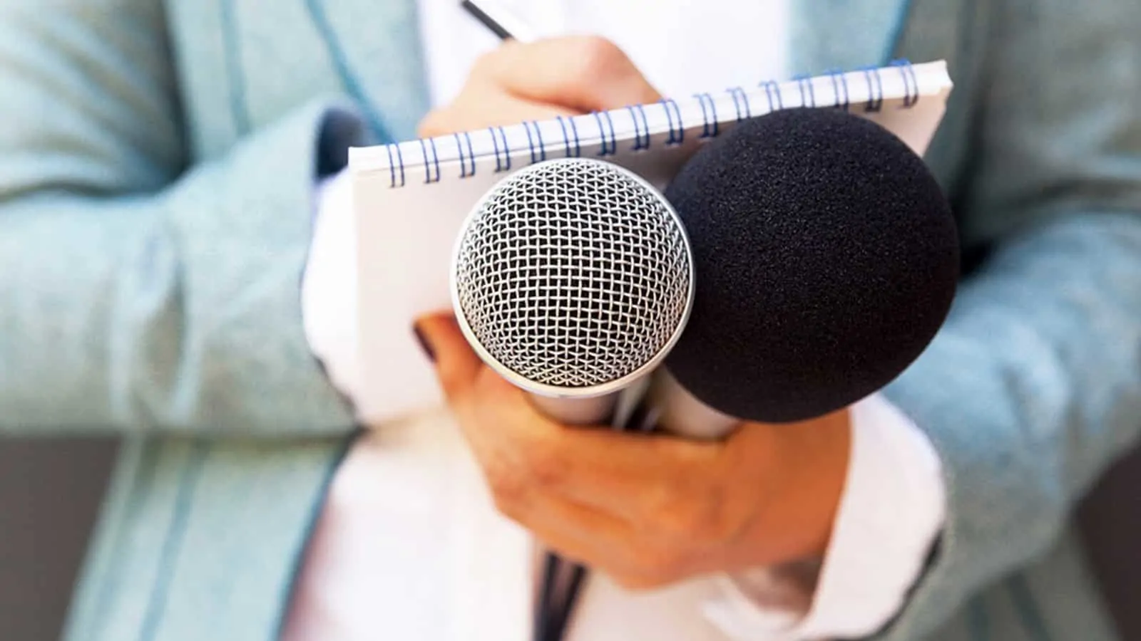 Dziennikarz trzyma dwa mikrofony i notatnik, przygotowując się do wywiadu.